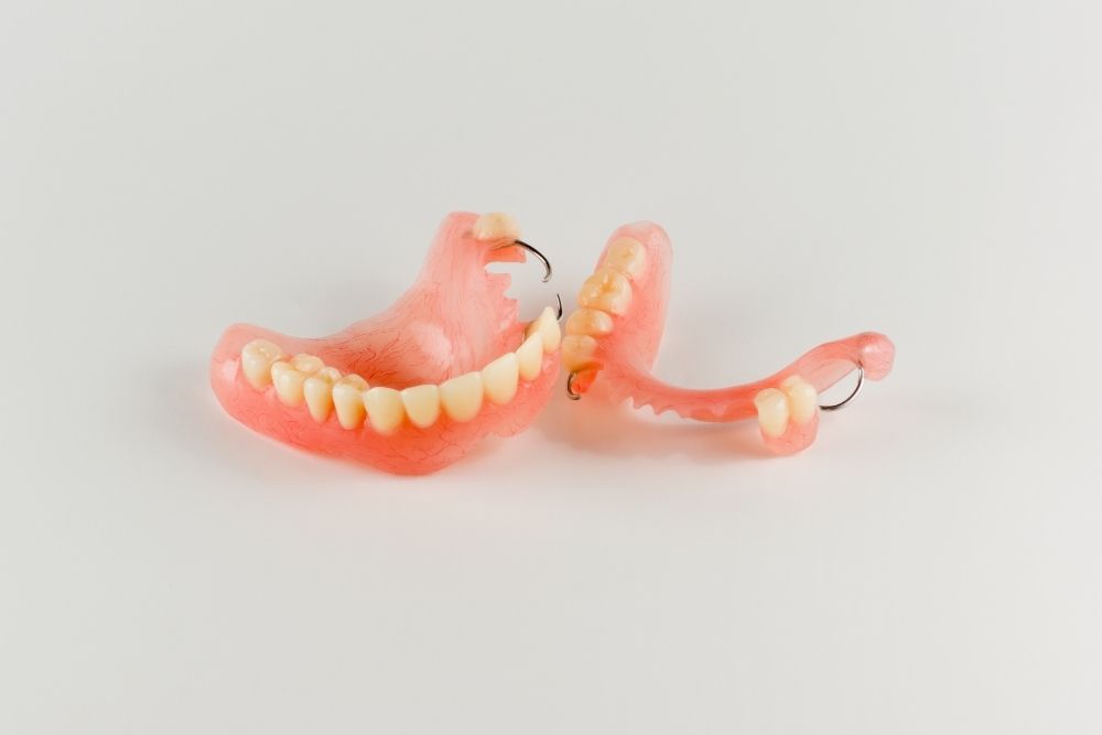 Dentures, pink with white teeth, on a white surface, top and bottom pieces separated.