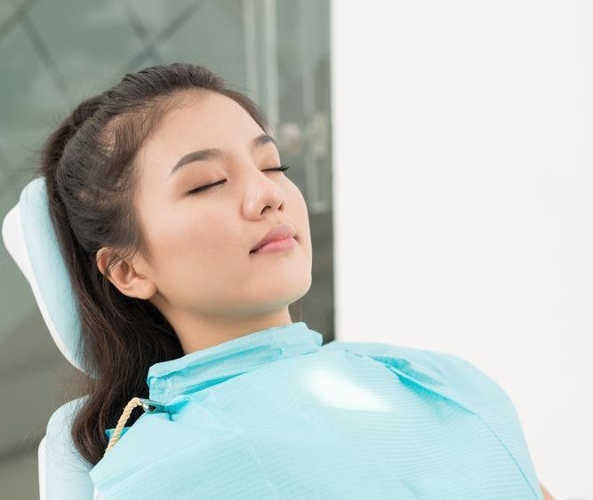 Woman with closed eyes in a dental chair, wearing a blue bib.