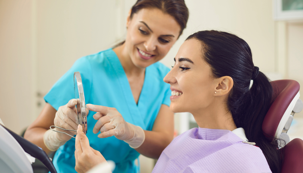 Dentist showing patient her teeth with a mirror in a dental office. Both smiling.