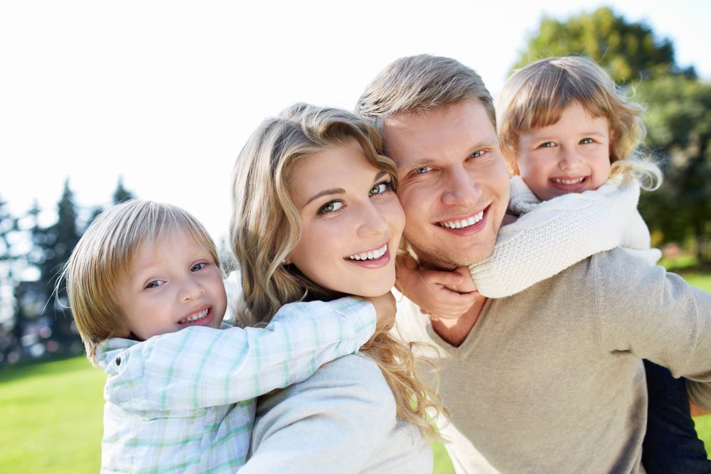 Happy family of four smiling outdoors: mother, father, and two children enjoying a sunny day.