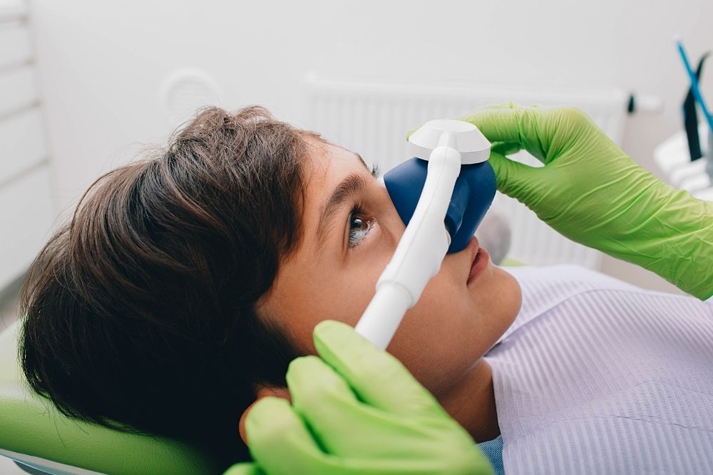 Boy receiving nitrous oxide at the dentist, blue mask, green gloves.