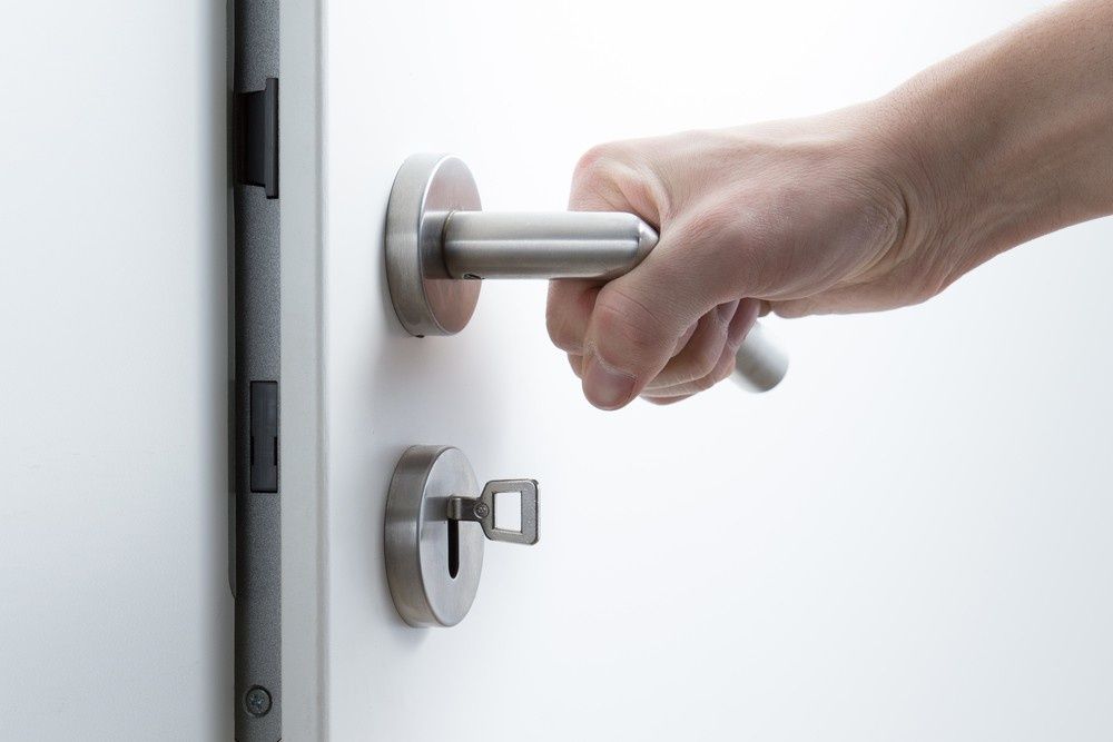 Hand Opening a White Door, Grasping the Silver Handle — NORTHCOAST LOCKSMITHS & SECURITY In Harrington, NSW