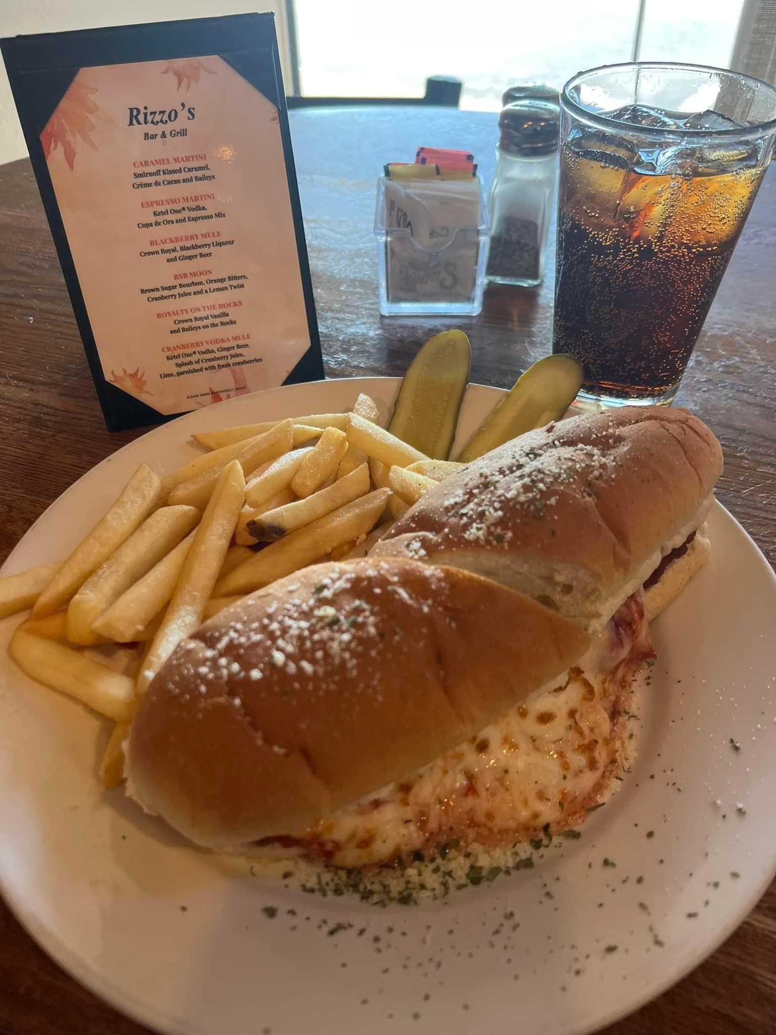 A sub sandwich with french fries and pickles on a plate.