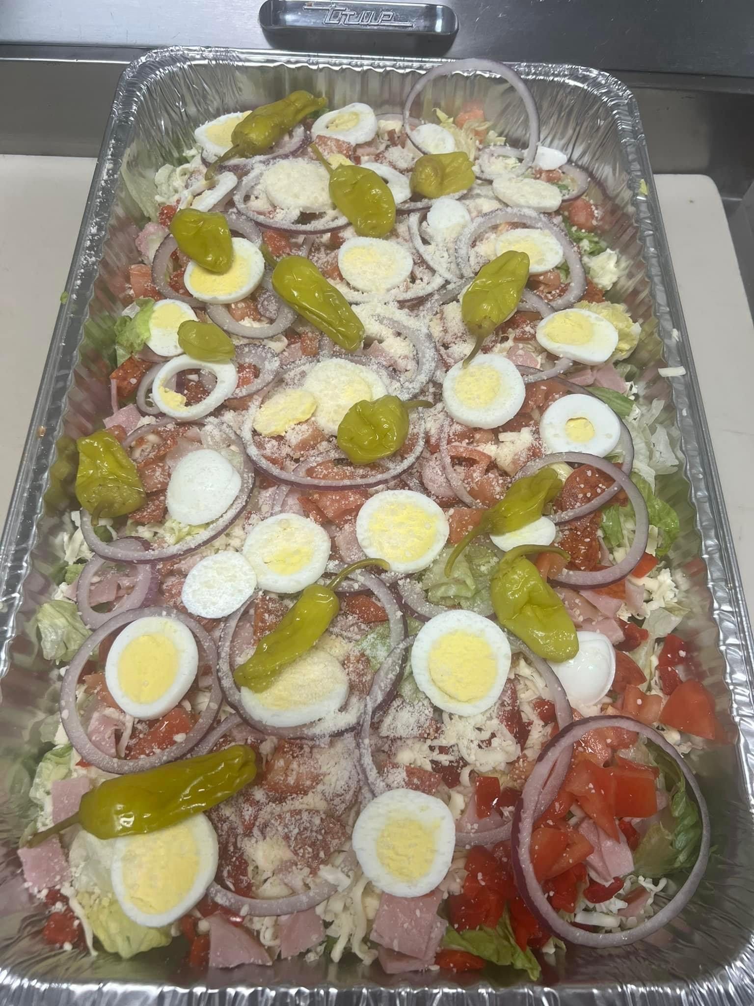 A large tray filled with a salad with eggs , peppers , onions and lettuce.