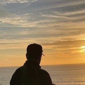 A man is standing on a cliff overlooking the ocean at sunset.