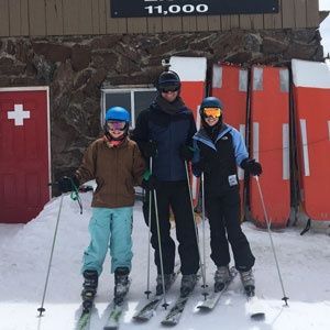 Three skiers are posing for a picture in front of a sign that says 11,000