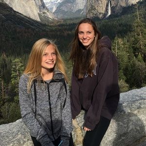 Two girls are posing for a picture in front of a mountain.
