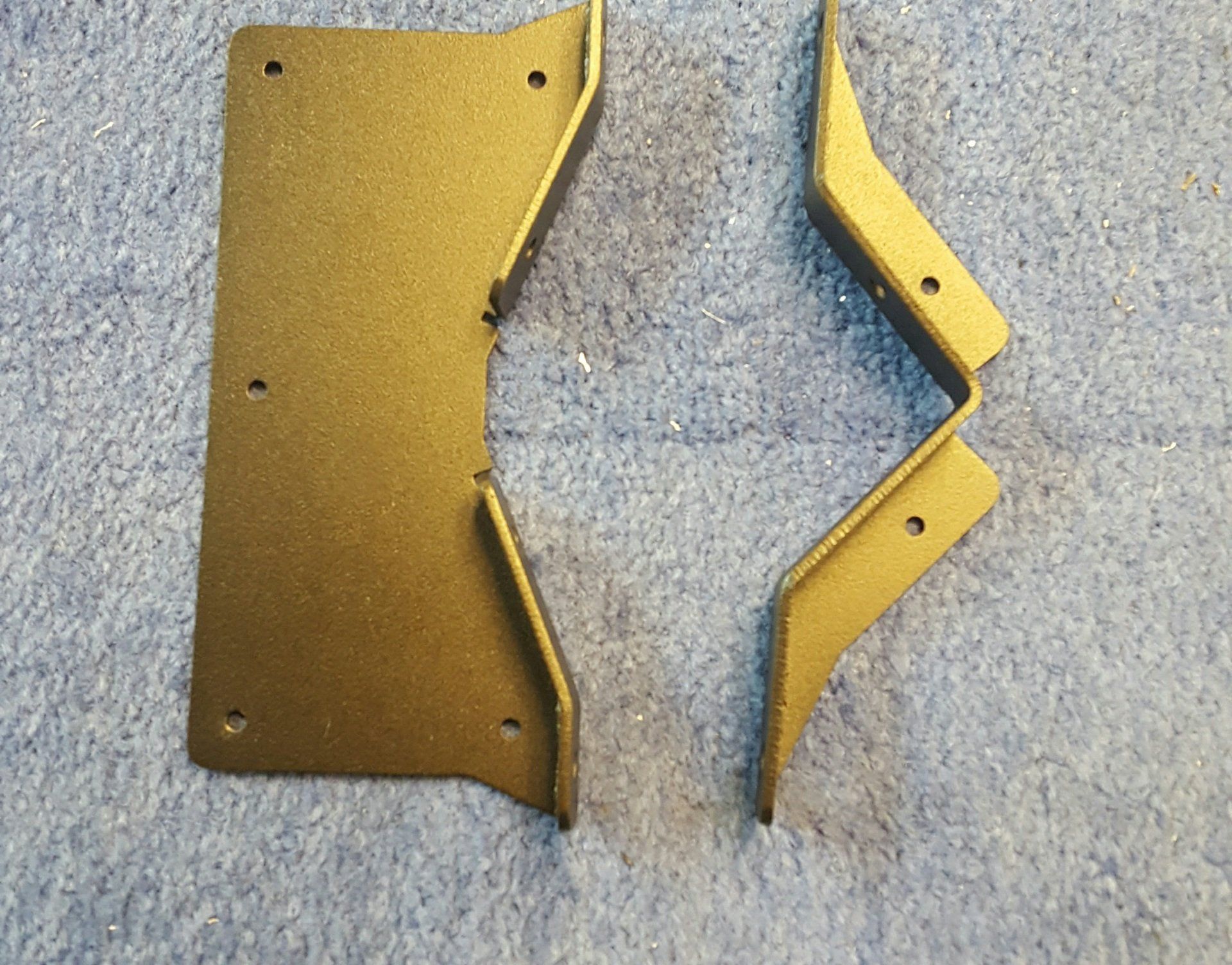 Two pieces of gold metal are laying on a carpet