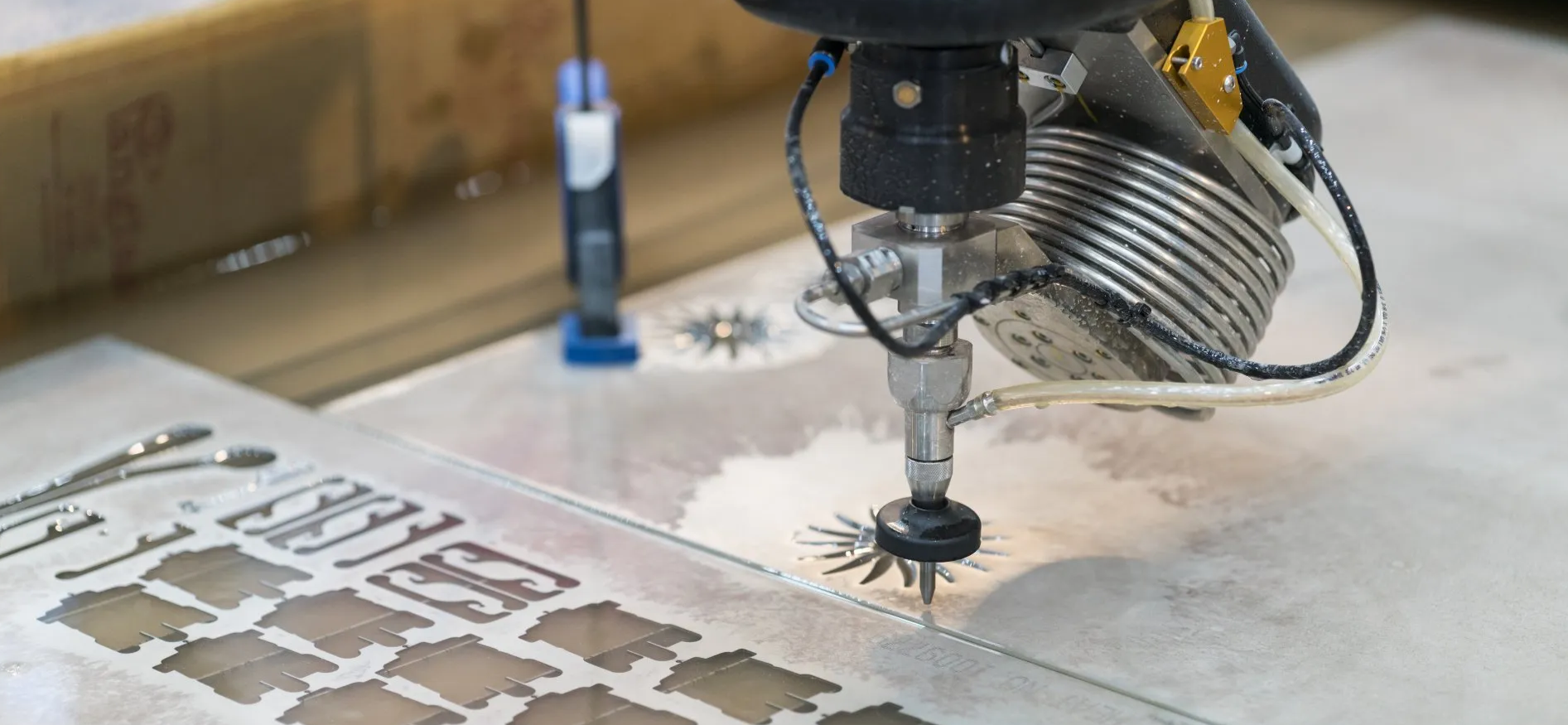 A close-up of a water jet cutter at work. The machine is cutting detailed designs from a sheet of material.