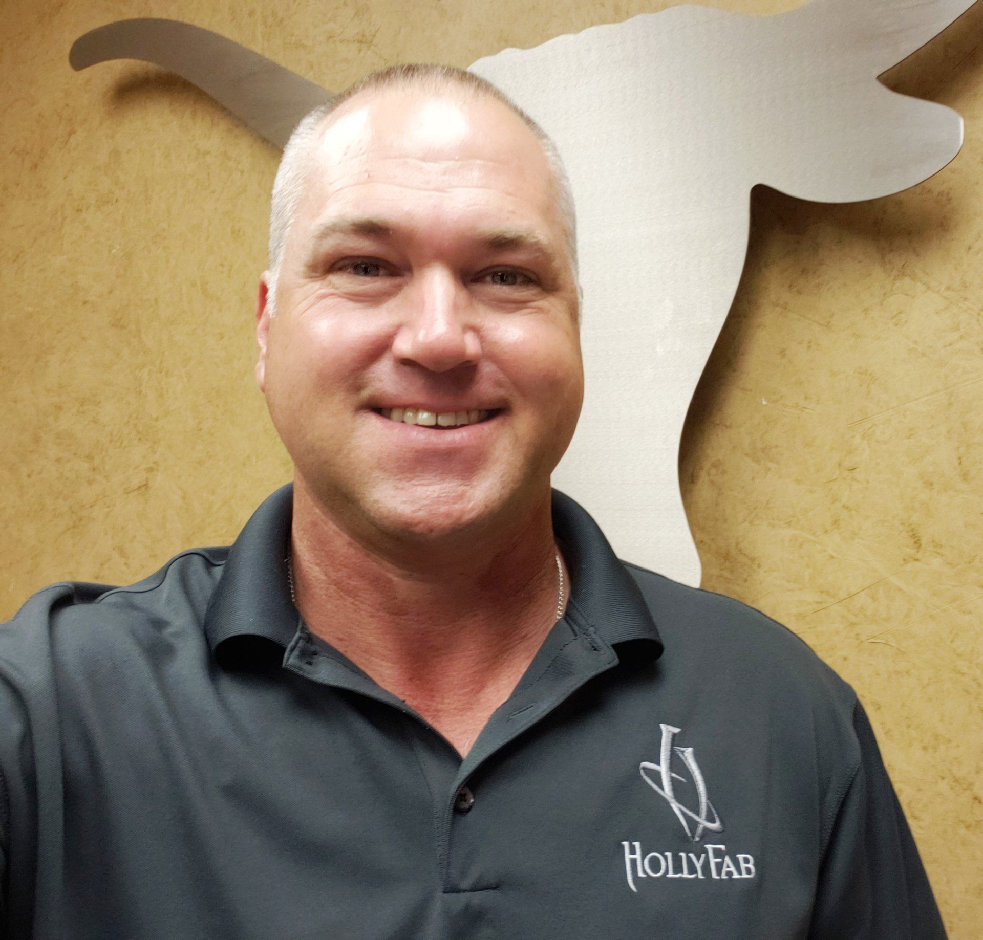 Man in gray shirt smiles in front of a metal Texas Longhorn sign, logo on shirt