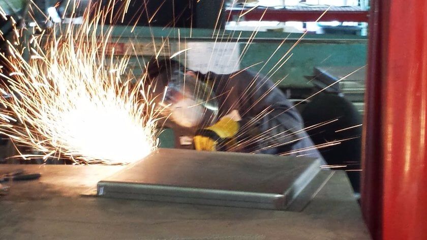 A man wearing a welding mask is welding a piece of metal.