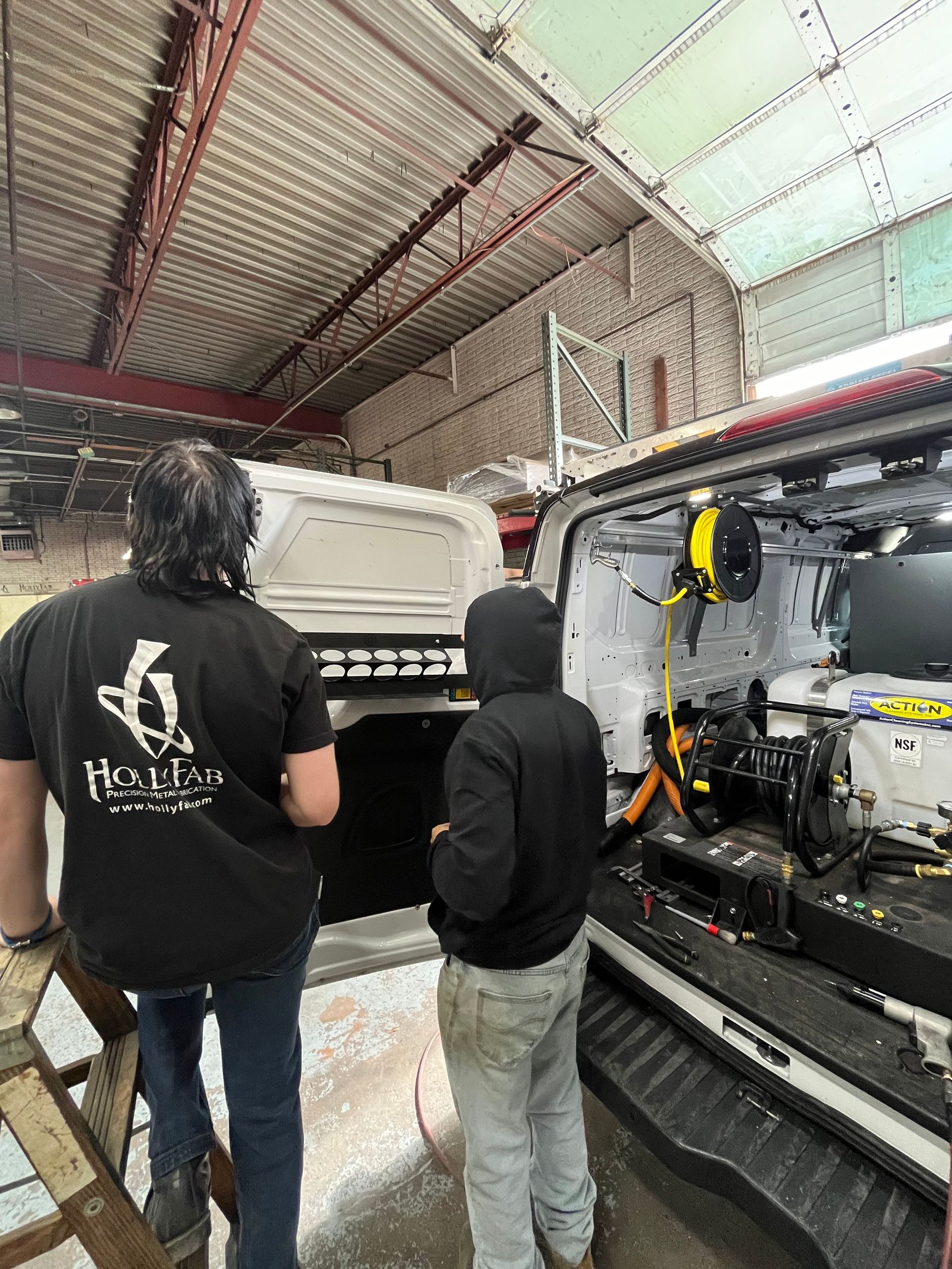 Two people inspecting a van interior in a workshop. The van has lights and a cable reel.