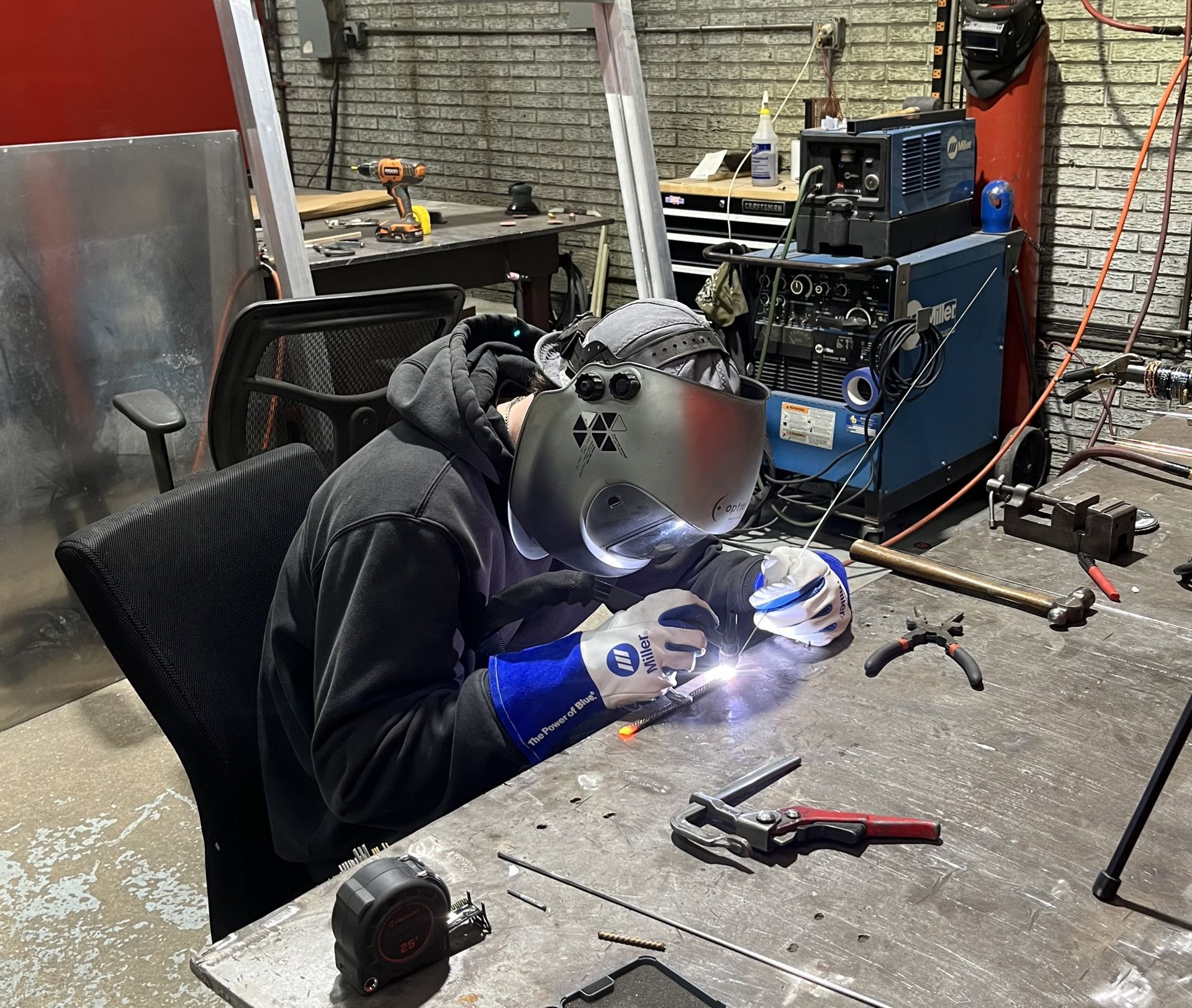 Welder in a workshop wearing a helmet and gloves, working on metal. Blue, black, gray colors.