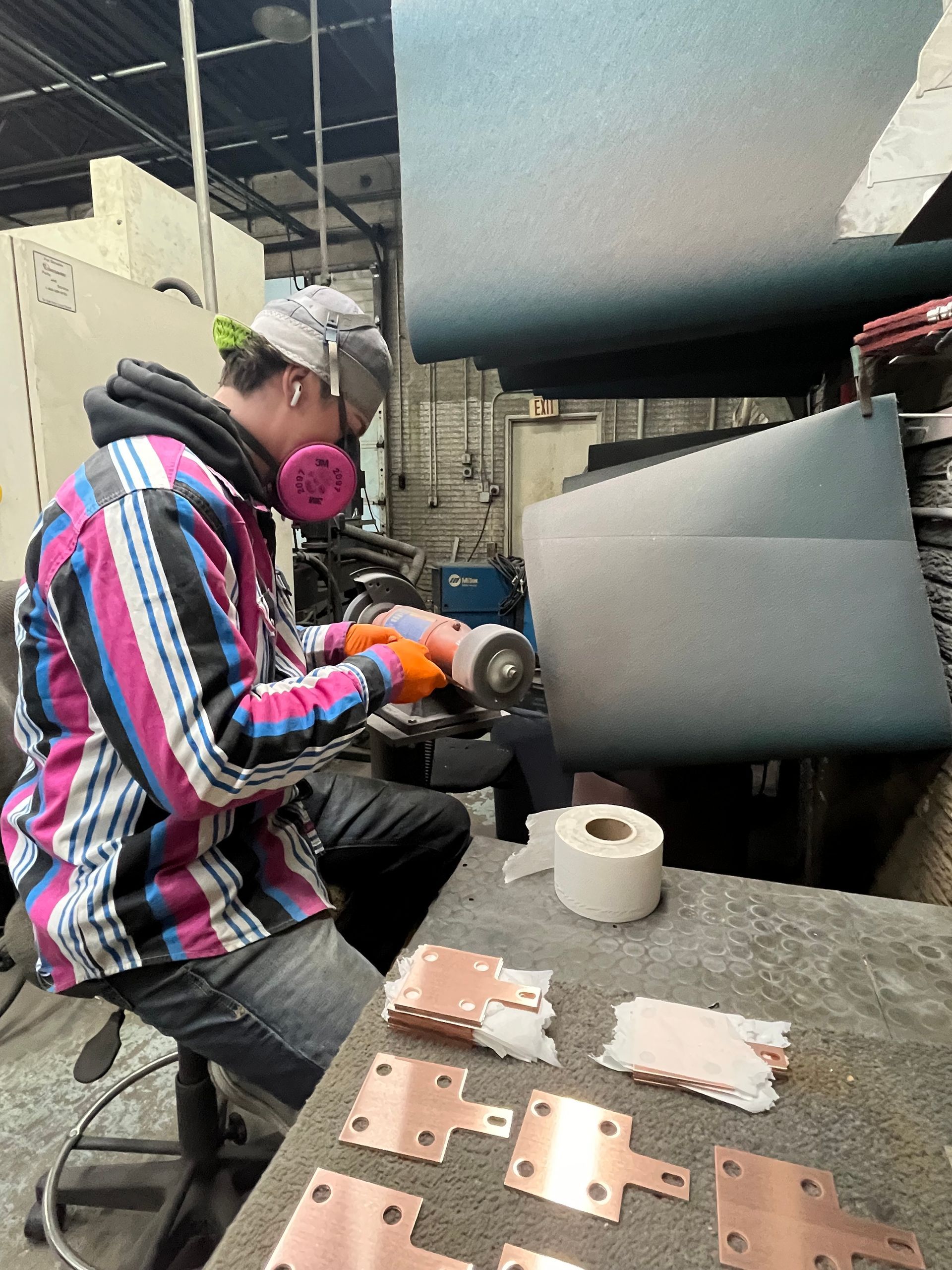 A person wearing safety gear grinds copper plates in a workshop.