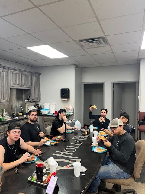 A group of people eating at a table in an office kitchen, smiling, enjoying lunch.