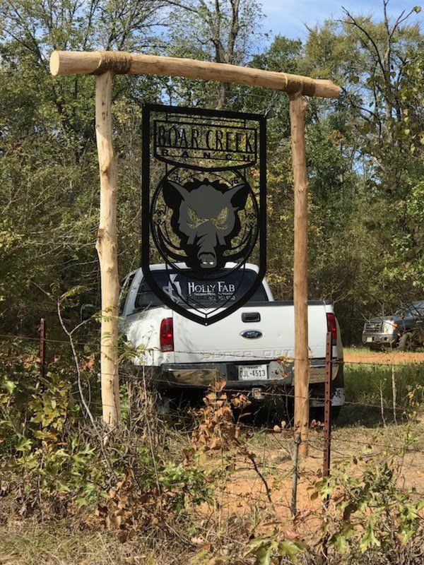 A white truck is parked in front of a sign in the woods.