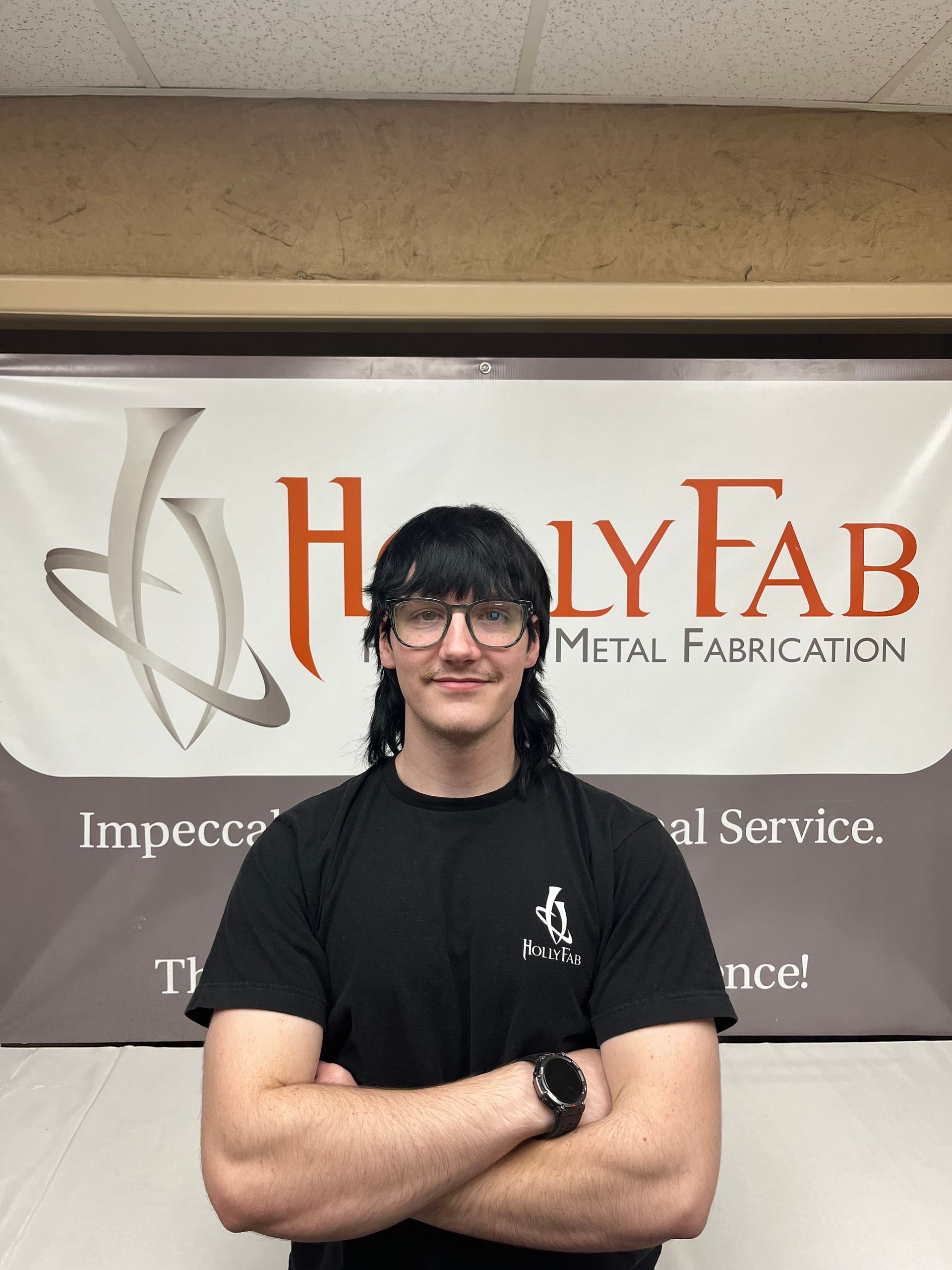 Young man with arms crossed, black shirt, standing in front of 