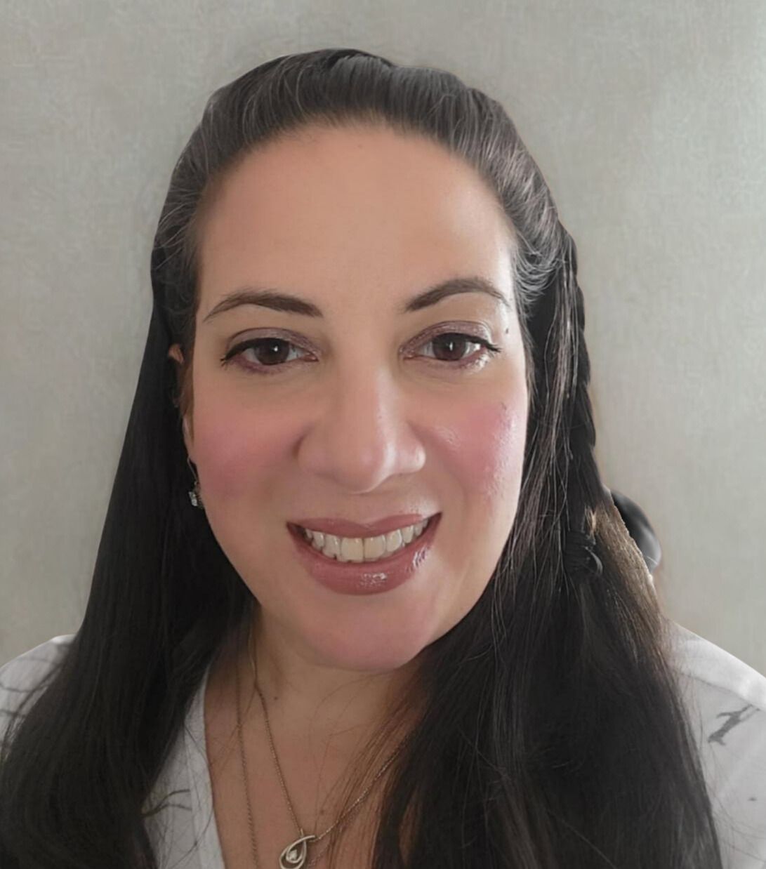 A young woman with long, curly blonde hair smiles at the camera. She wears a black top and a gray blazer.