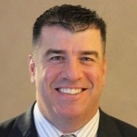 A smiling man with short, dark hair in a suit and tie. He's looking directly at the camera.