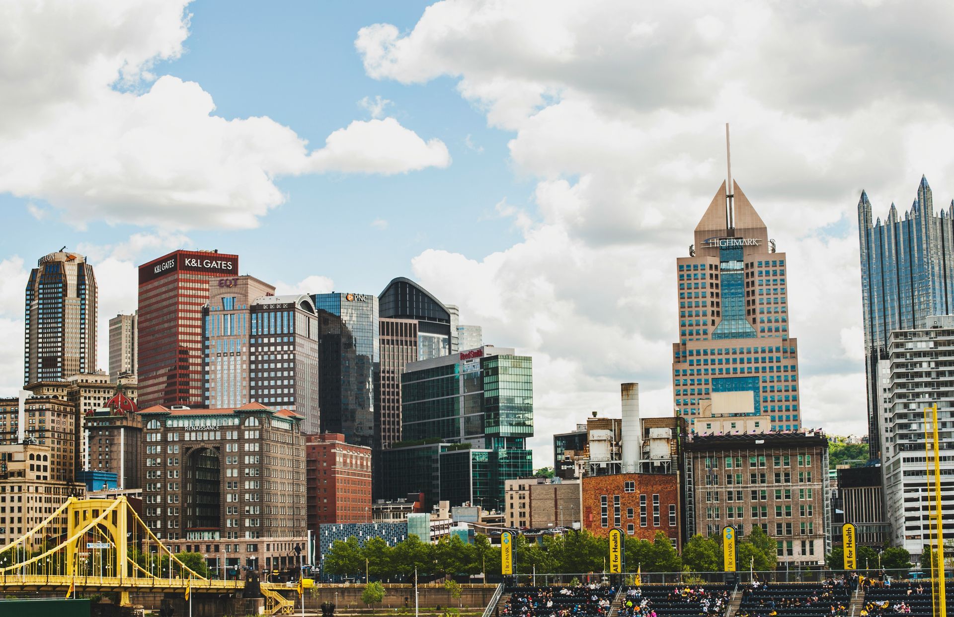 City skyline with mix of architectural styles under a cloudy sky. Includes a yellow bridge and various office buildings.