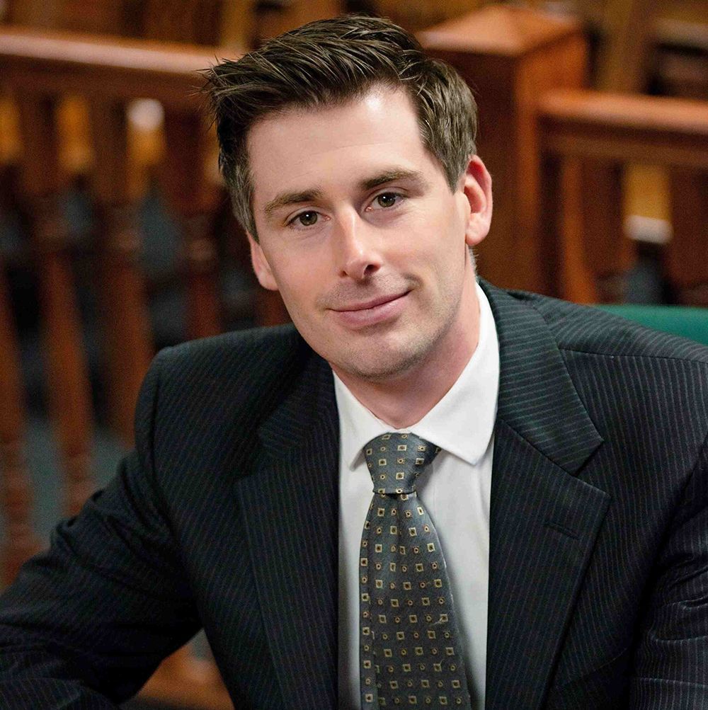 Man in suit smiling, indoors, possibly a courtroom.