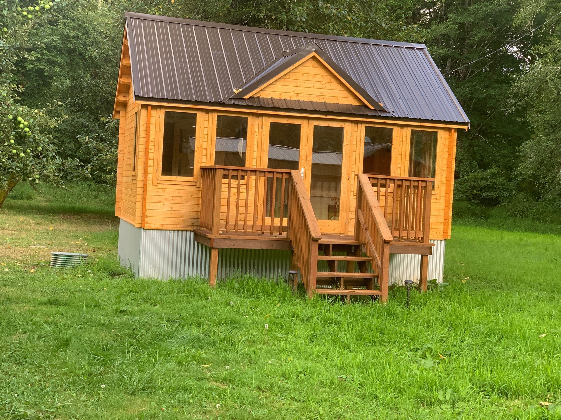 A small wooden house with a porch and stairs in a grassy field.