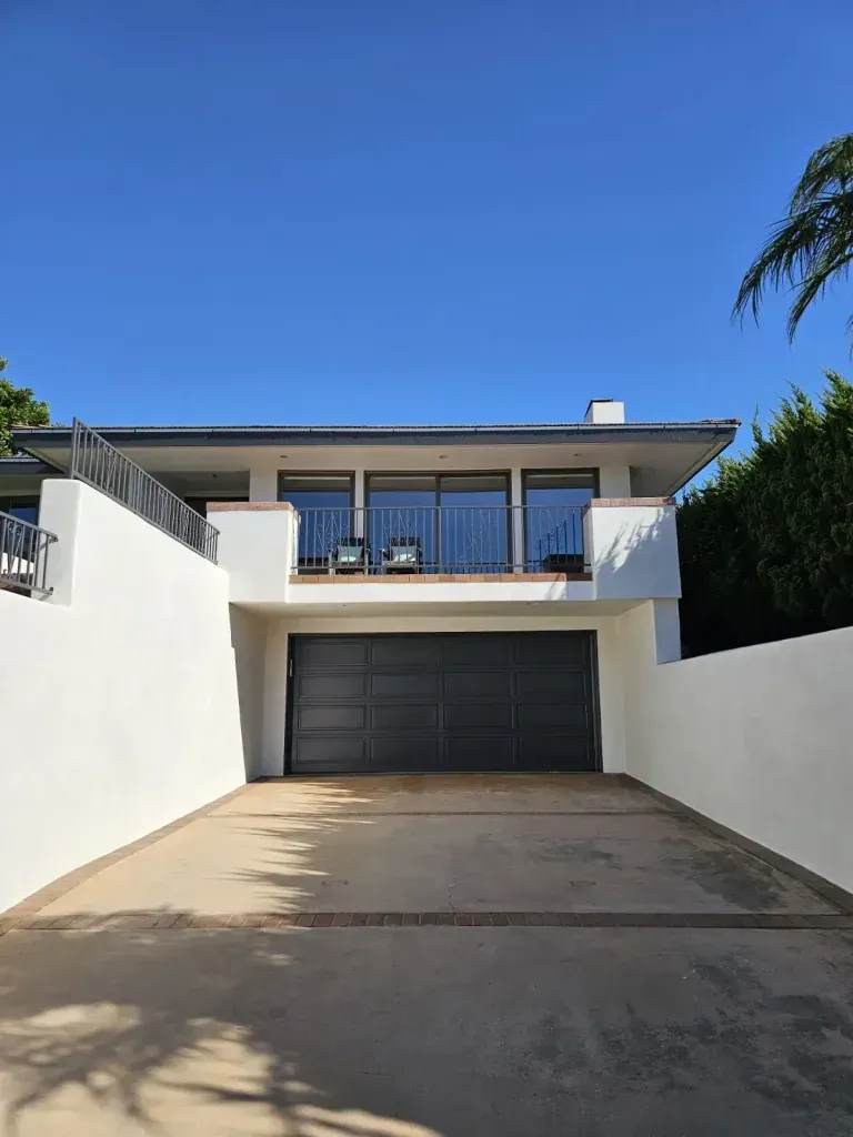 Modern white two-story house with a dark garage door and driveway under a clear blue sky