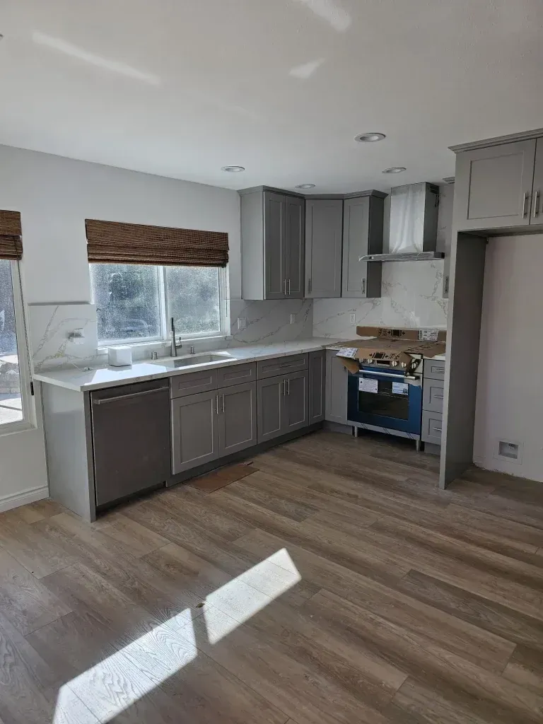 Modern kitchen with gray cabinets, wood floor, window blind, and blue stove beneath a range hood.