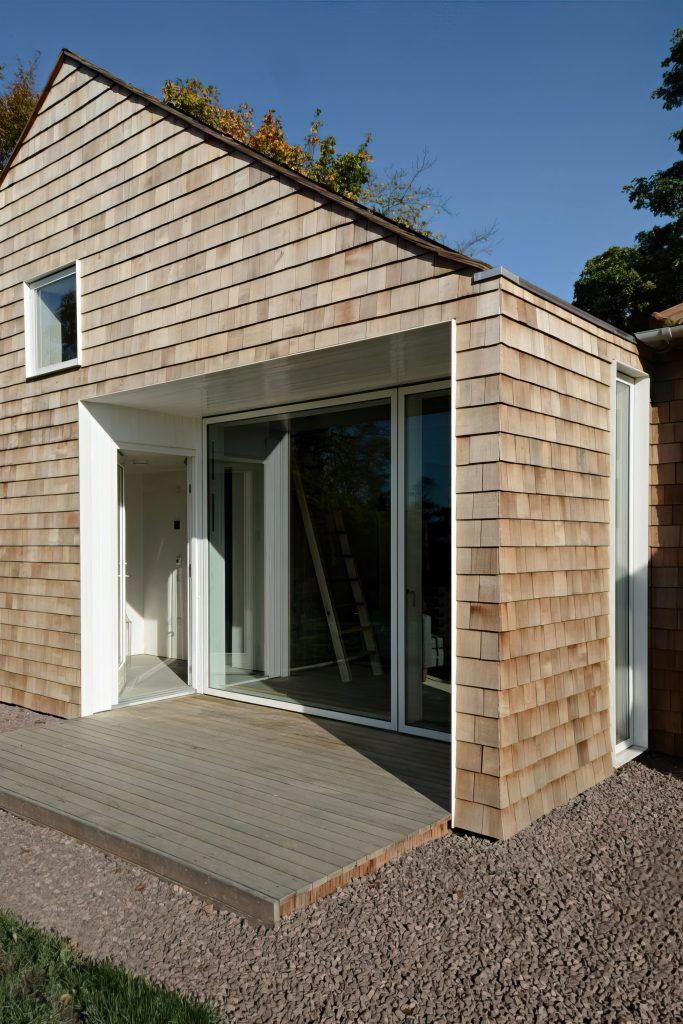 Modern house exterior with sloped roof, wood cladding, and large sliding glass doors opening to a patio.