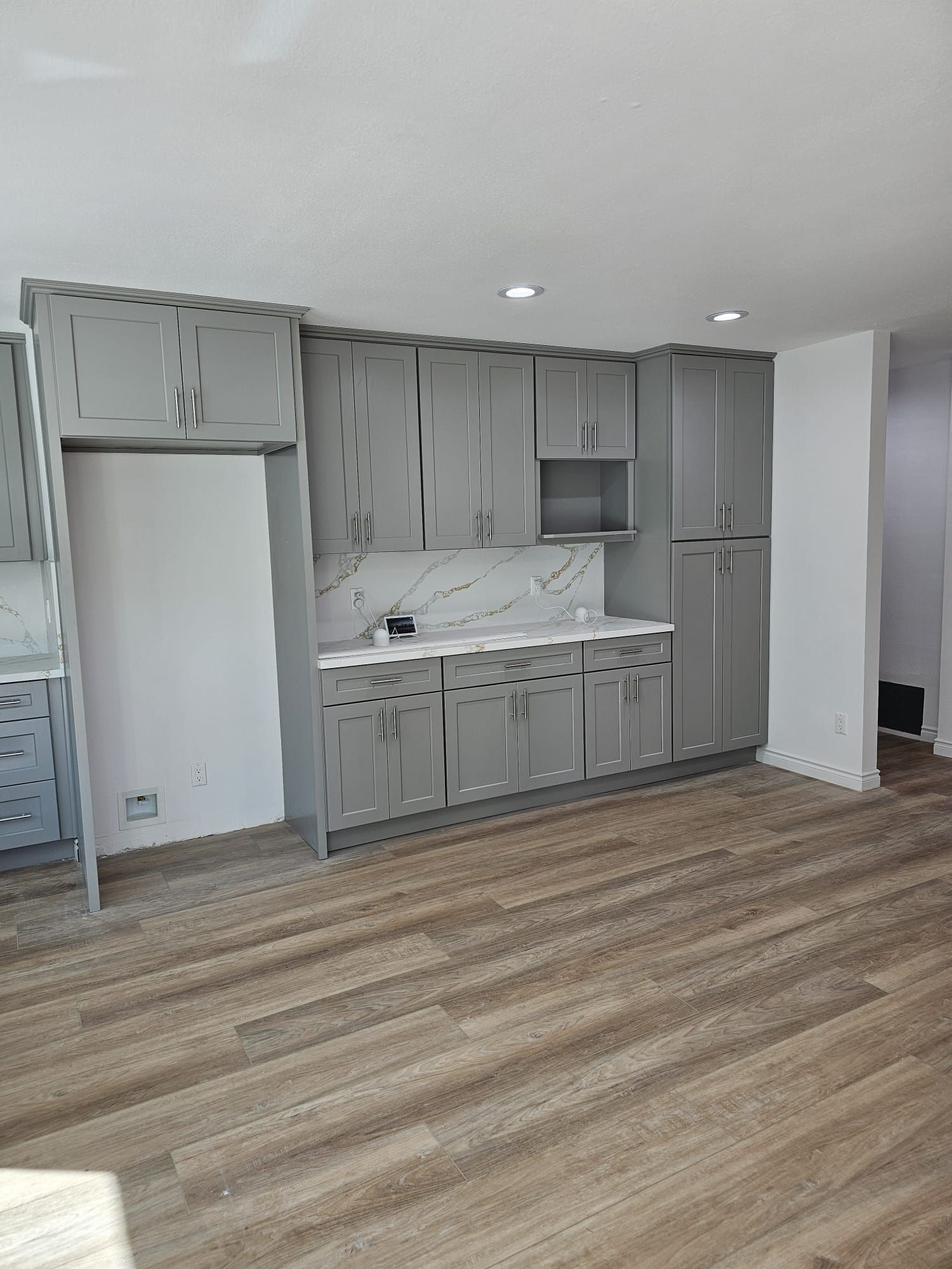 Empty kitchen with gray cabinets, white countertops, and wood-look flooring in a bright room