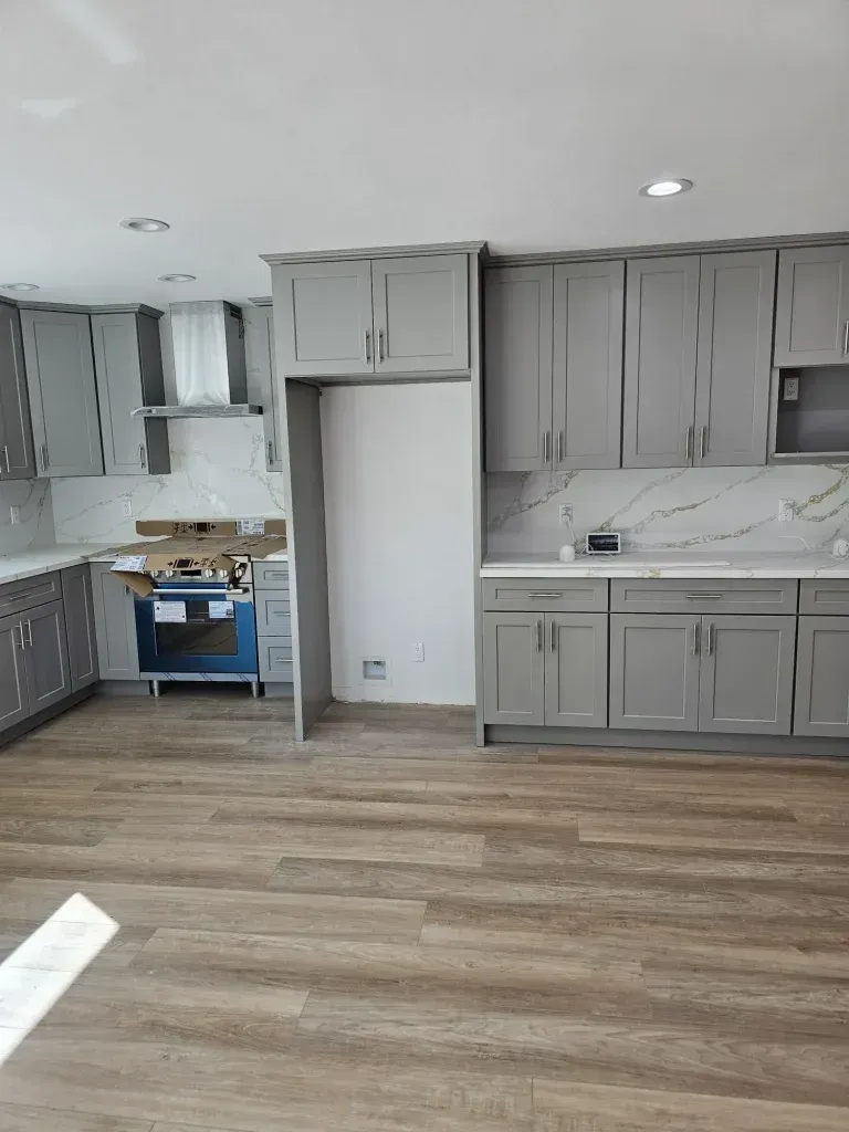 Empty modern kitchen with gray cabinets, white countertops, and light wood flooring.