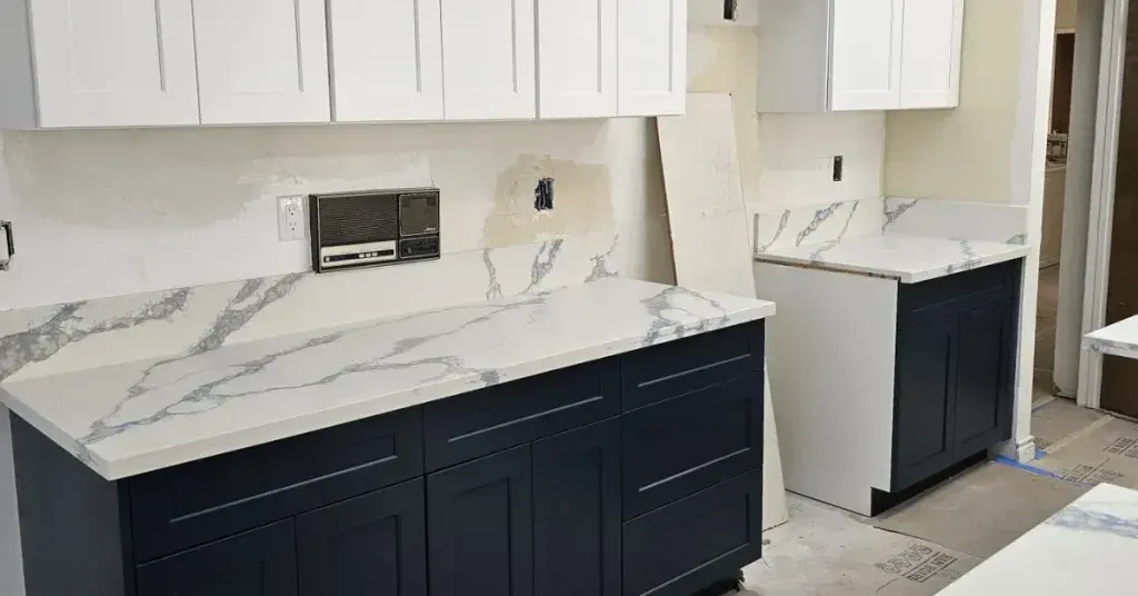 Modern kitchen with white marble countertops, navy cabinets, and a large island under white upper cabinets