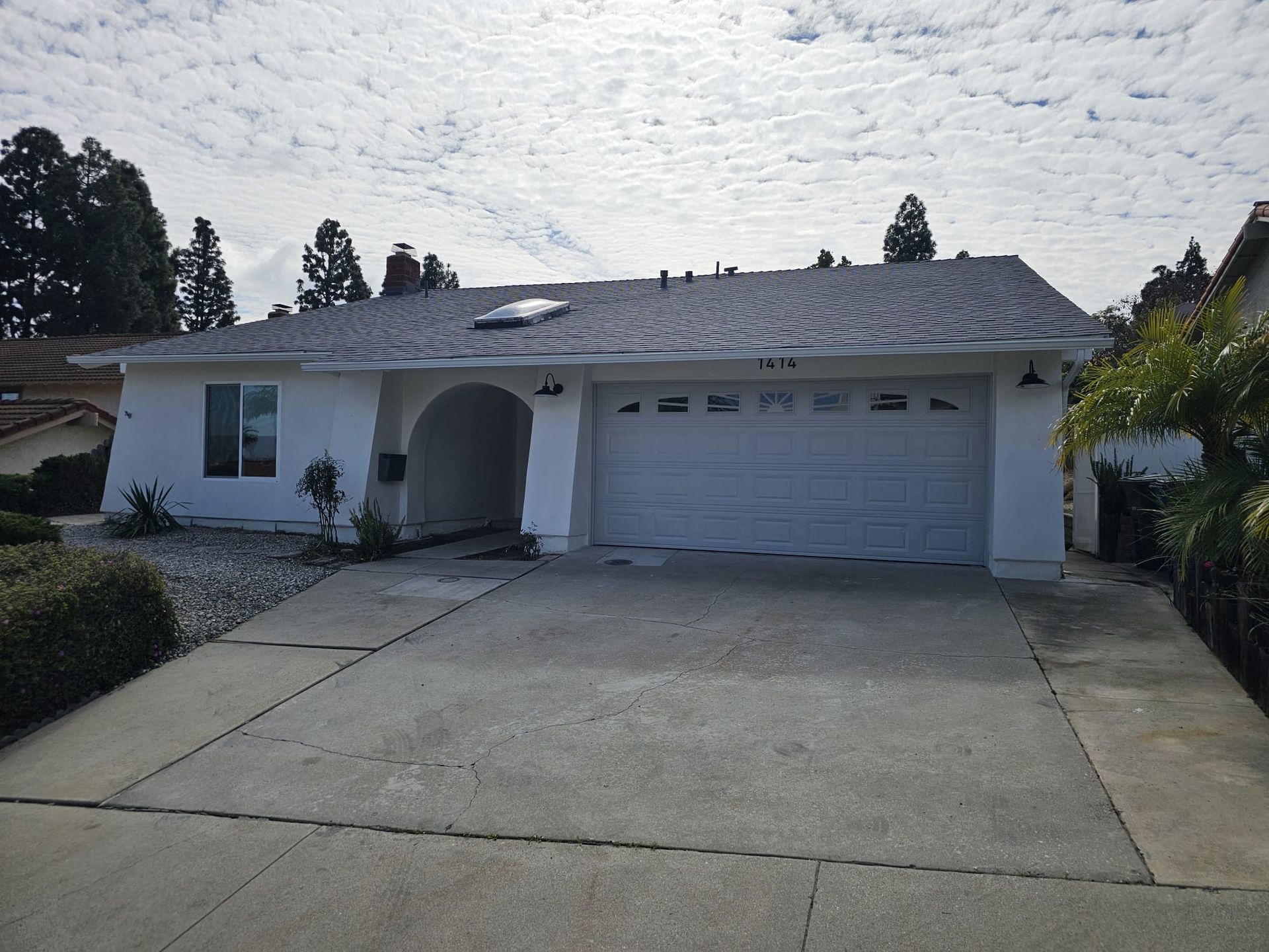 Single-story suburban house with white exterior, arched entry, two-car garage, and concrete driveway