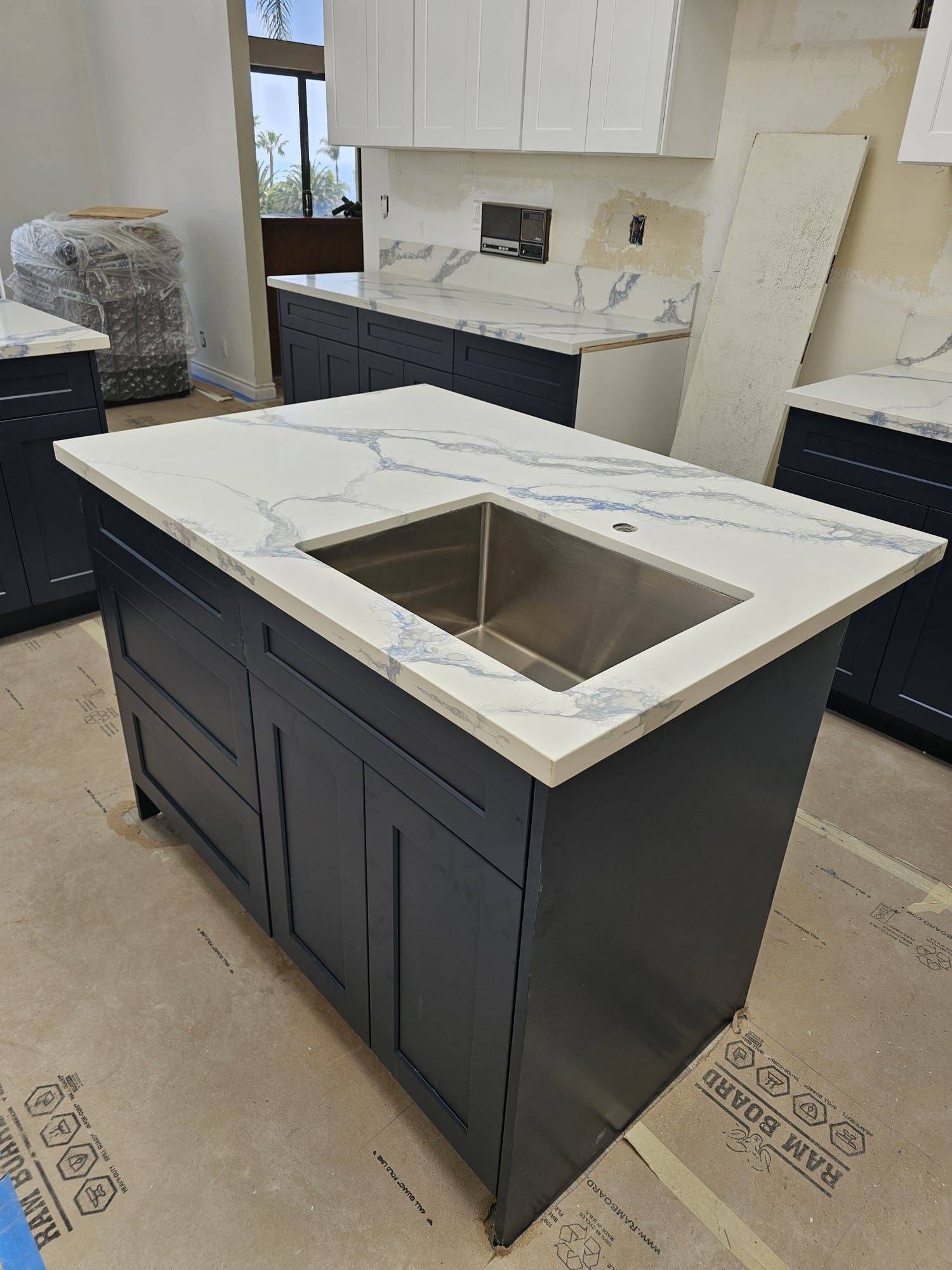 Kitchen island with dark cabinets and white marble countertop, featuring a stainless sink in a showroom.