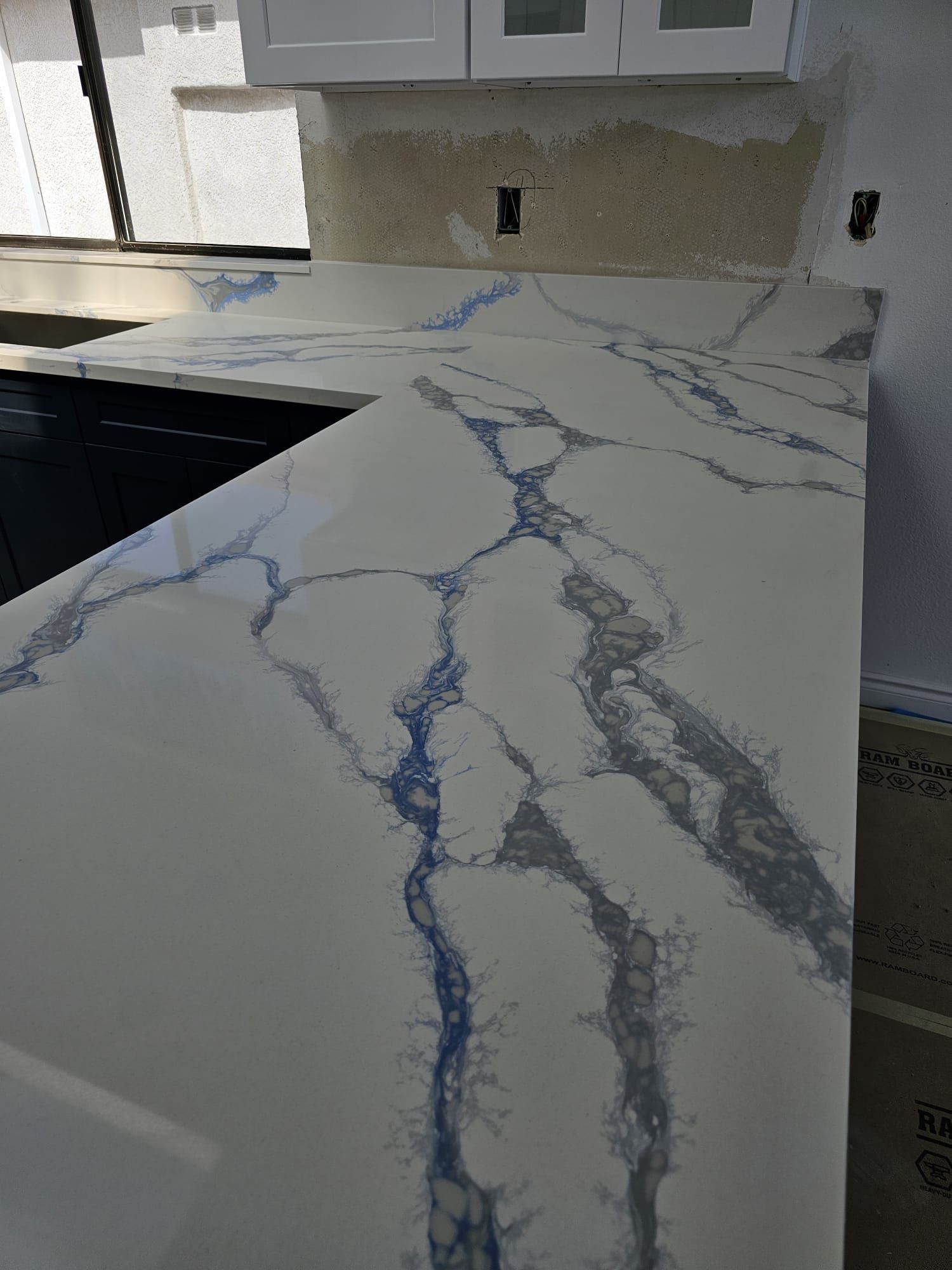 Kitchen countertop with white marble-look surface and blue-gray veining beside a black sink.