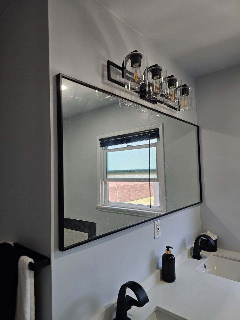 Bathroom vanity with a large mirror reflecting a window and shelf decor above the sink.