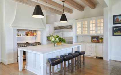 Bright white kitchen with island, black bar stools, pendant lights, and exposed wood beams
