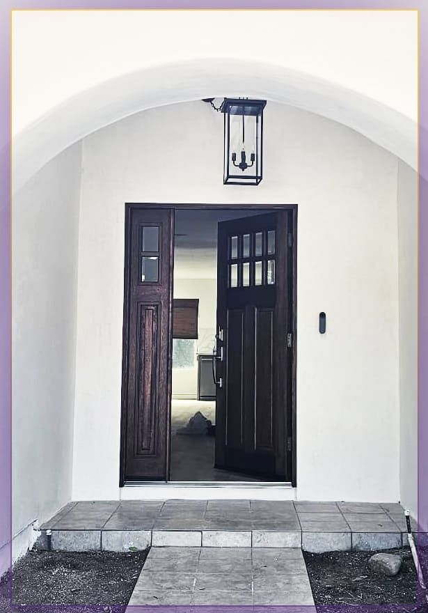 Front entrance with open dark wooden door under a white arch, showing a lantern overhead and tiled steps.