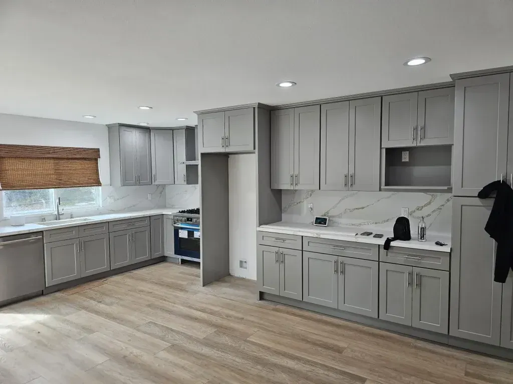 Empty gray kitchen with light wood floors, white countertops, and a window with a woven shade.