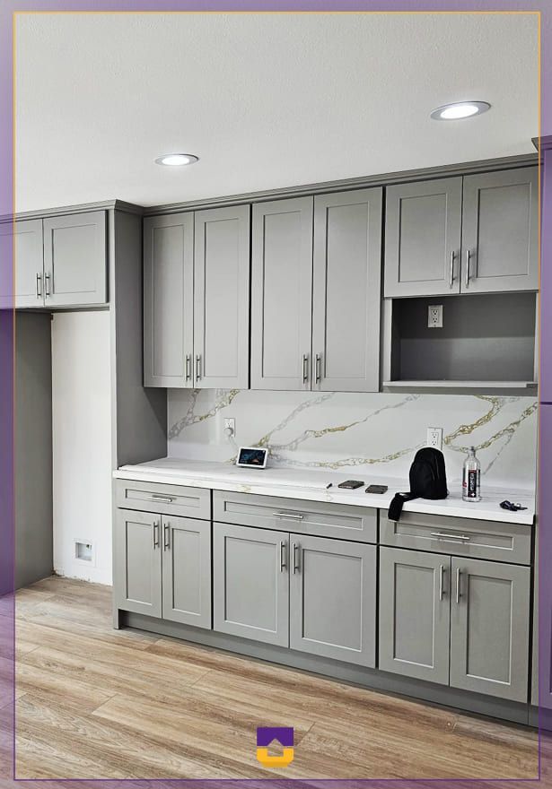 Gray modern kitchen with marble backsplash, upper and lower cabinets, white countertop, and recessed lights