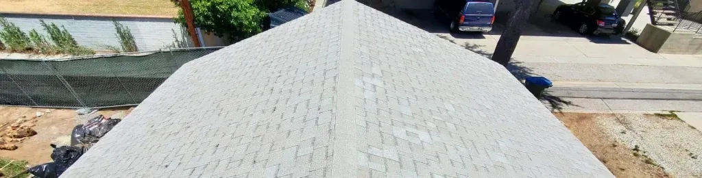 A textured white roof or large structure viewed from above, with a driveway and street visible beyond.