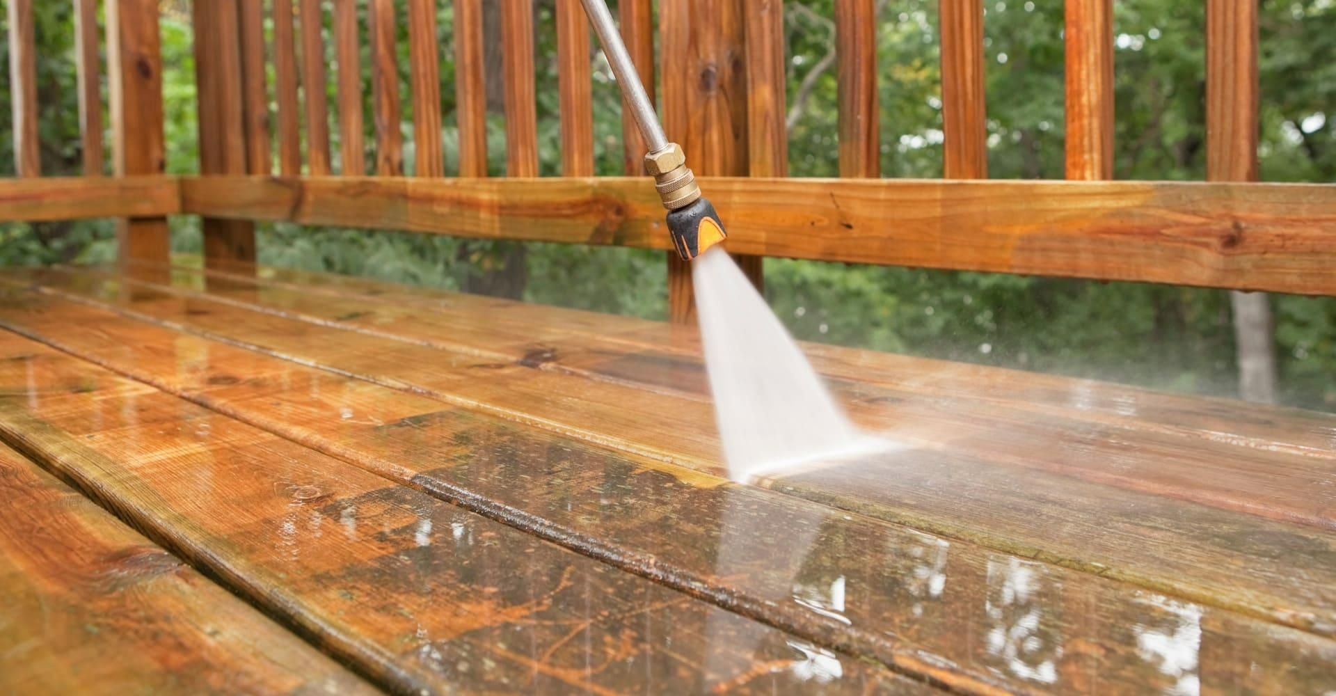 Power washer cleaning a wooden deck, spraying water, removing grime.