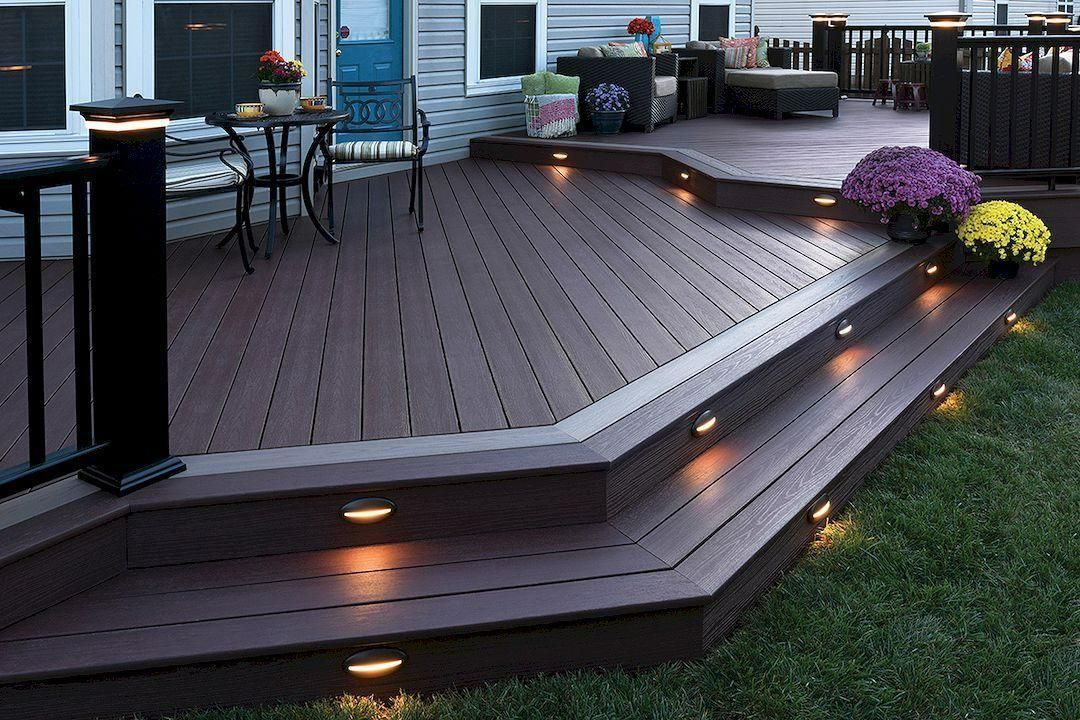 Multi-level wooden deck with built-in lighting and steps, next to green grass.