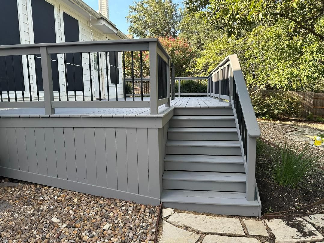 Gray deck with stairs leading to it, surrounded by foliage.