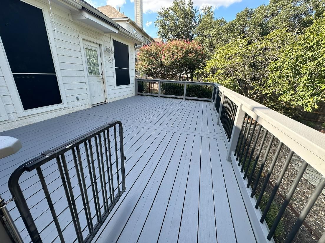Wooden deck with white railing and black metal bars. Exterior view near trees and a house.