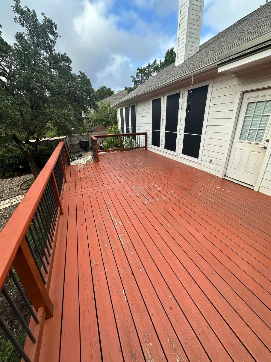 Red-stained wooden deck attached to a white house with black shutters and a cloudy sky.