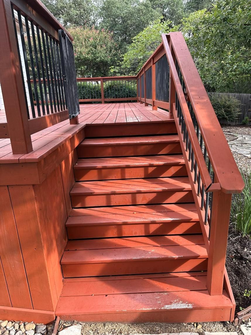 Red wooden deck with steps leading up, black railing on left, set outdoors.
