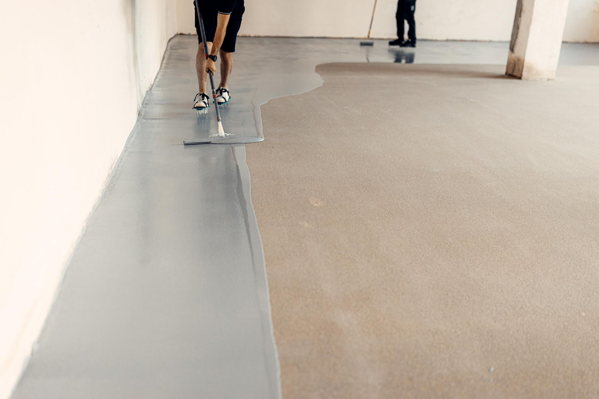 Workers applying gray epoxy flooring in an unfinished interior.