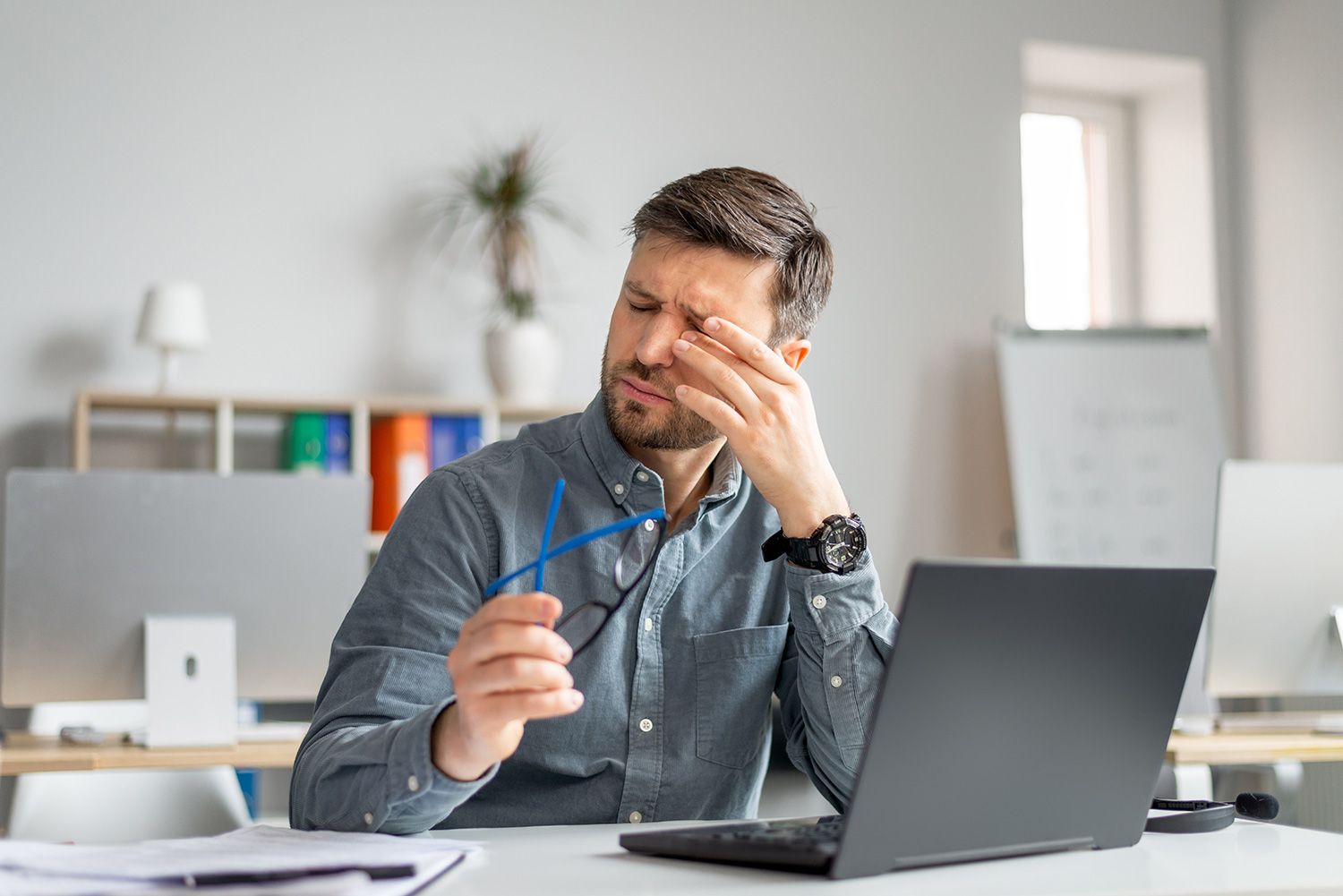 Man at desk with laptop rubbing his eye
