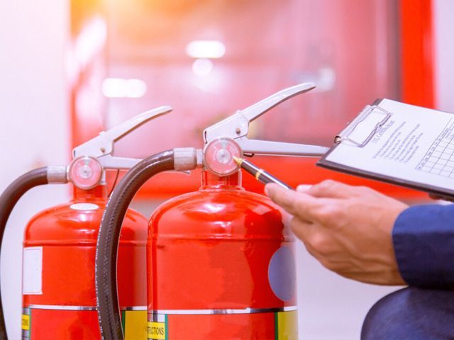 A Man Is Holding A Clipboard And Pointing At A Fire Extinguisher — Certcorp DGL in Bundaberg South, QLD